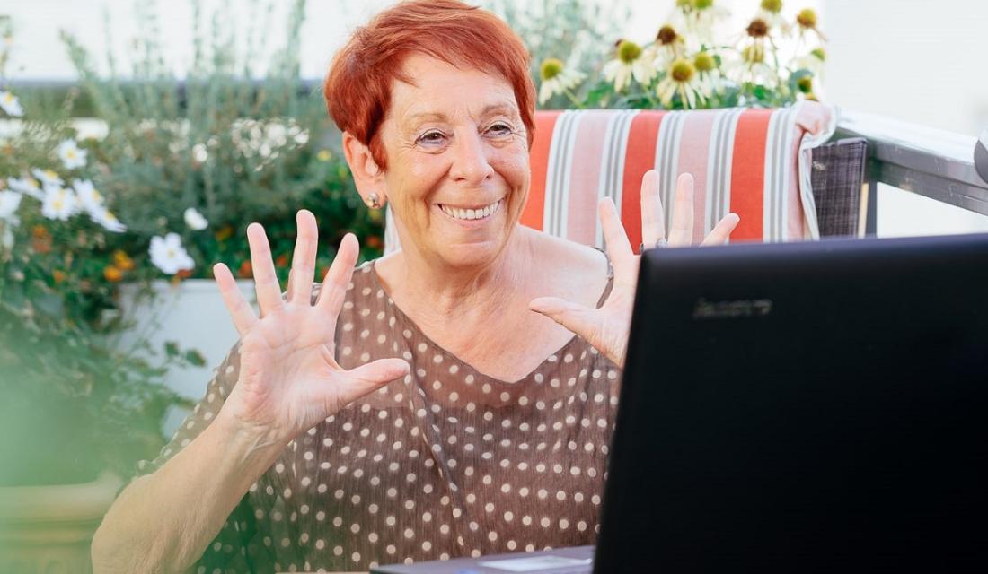 Ältere Frau sitzt vor ihrem Laptop und hebt die Hände.
