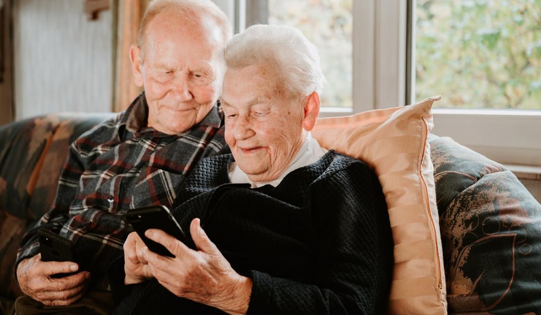 Älteres Ehepaar sitzt auf der Couch mit Smartphones in der Hand.