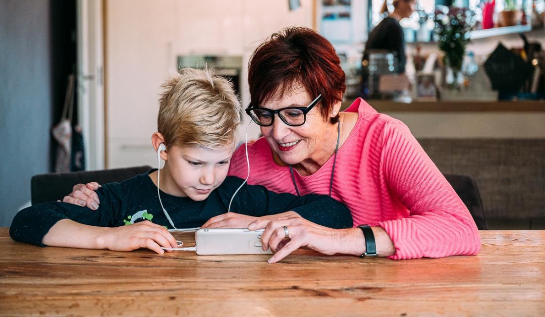 Frau sitzt mit Enkel an einem Tisch und sie spielen mit dem Smartphone.