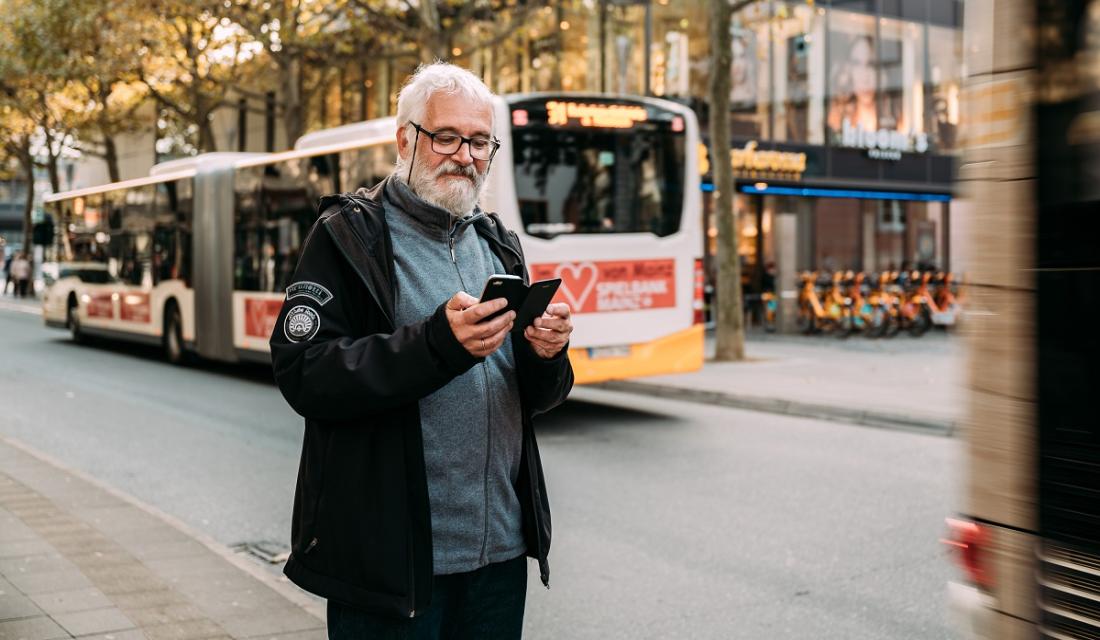 Mann mit Smartphone an einer Bushaltestelle.