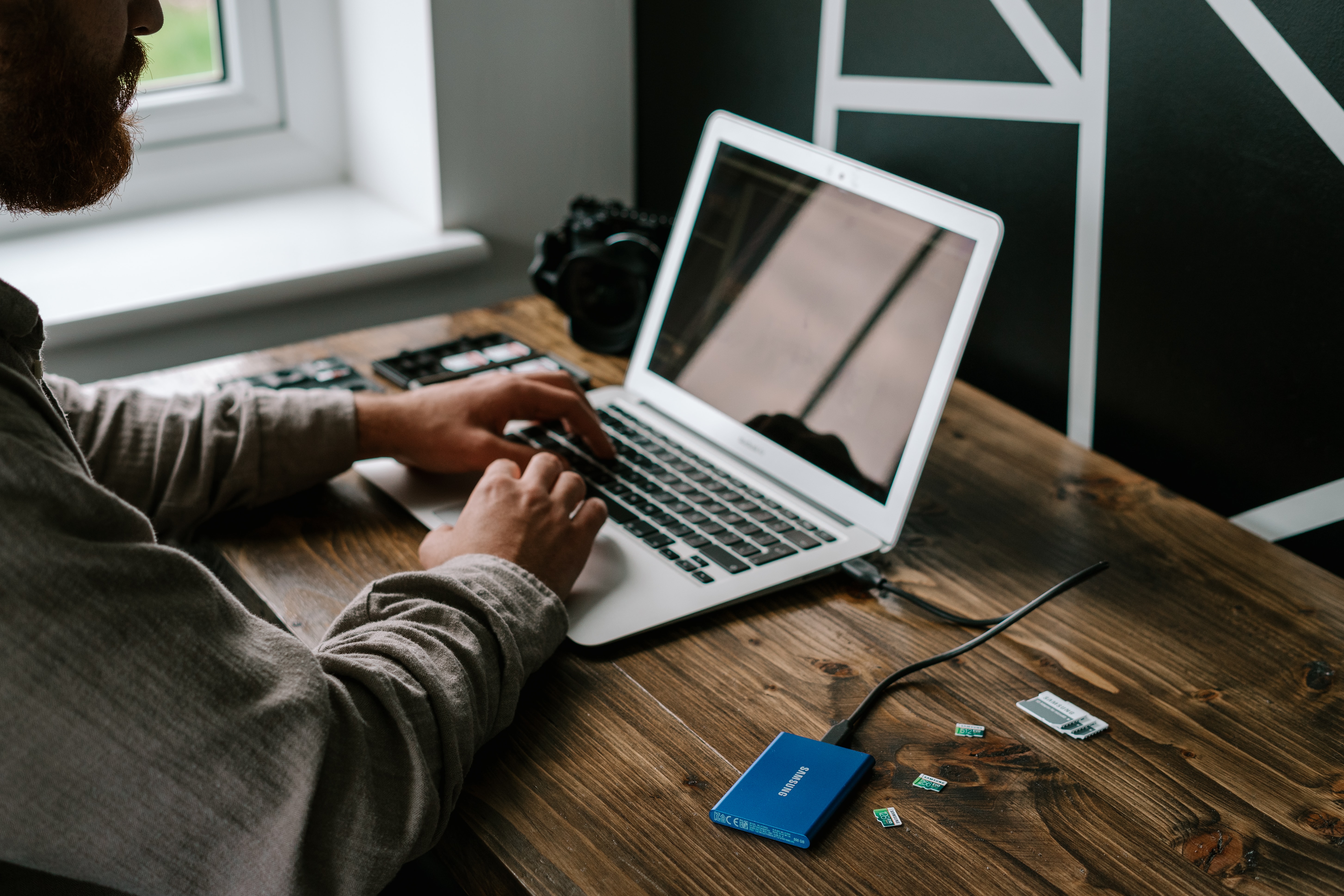 Ein Mann sitzt vor einem Laptop, an dem eine externe Festplatte angeschlossen ist. Neben der Festplatte liegen verschiedene Speicherkarten.