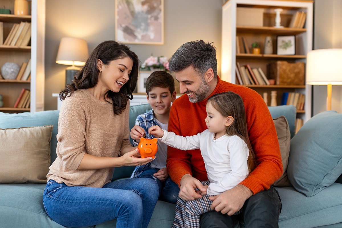 Eine Familie auf dem Sofa füttert ein Sparschwein mit Geld