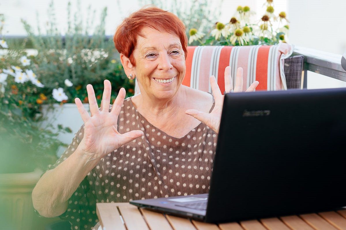 Eine ältere Frau sitzt fröhlich vor ihrem Laptop. 