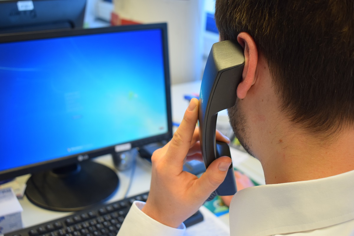 Mann sitzt am PC und hat den Telefonhörer am Ohr.