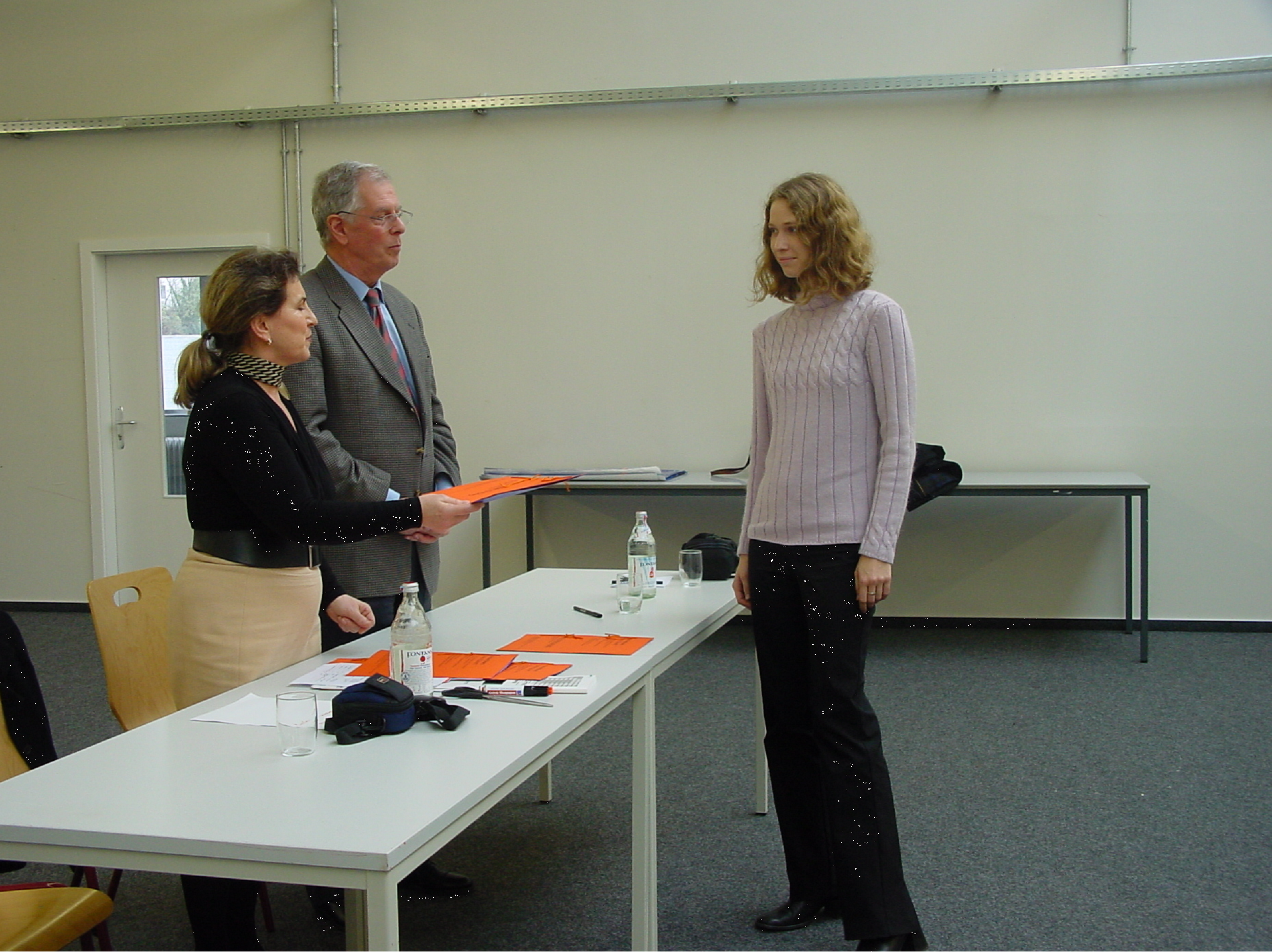 Ein Mann und eine Frau überreichen eine Urkunde an eine Studentin.