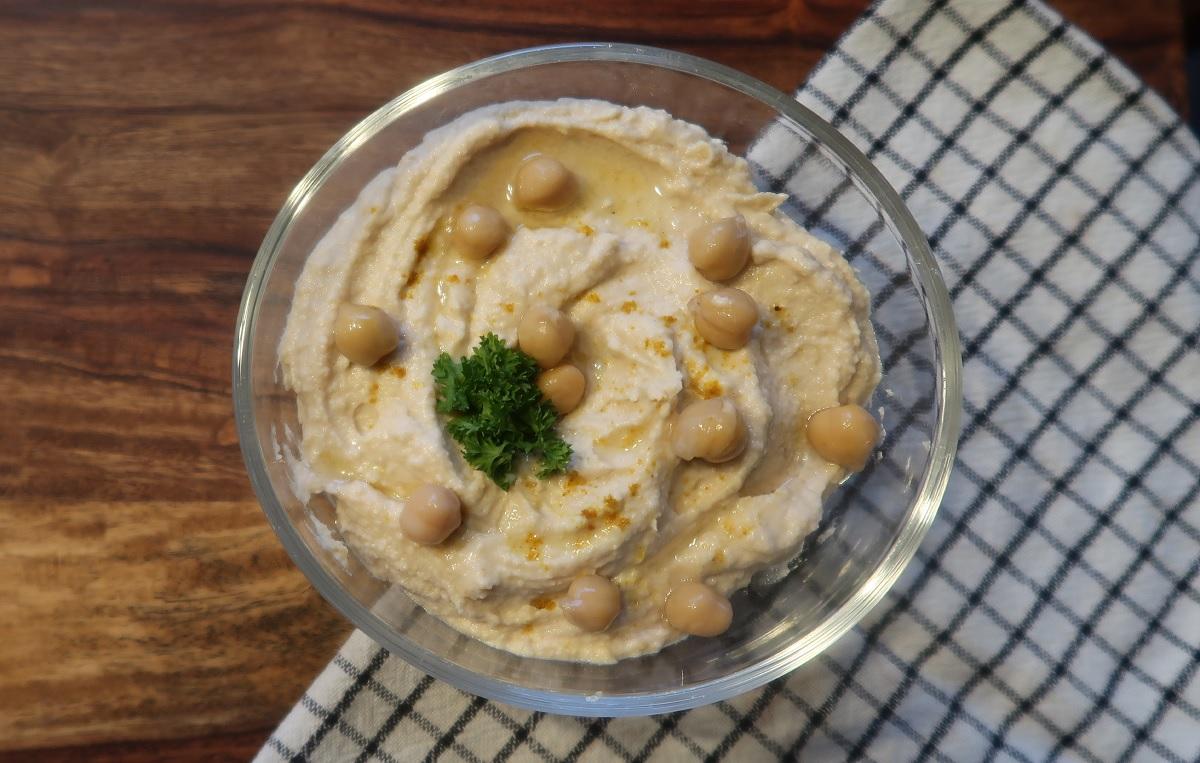 Eine Schale mit Hummus. Es liegen noch Kicherebsen und Petersilie als Dekoration auf dem Hummus.