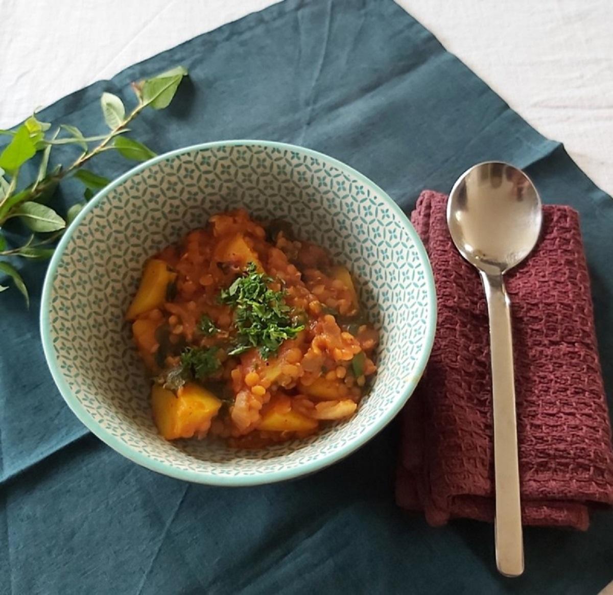 Eine Schale mit Linsen-Kartoffel-Curry auf einem Tisch mit Besteck.