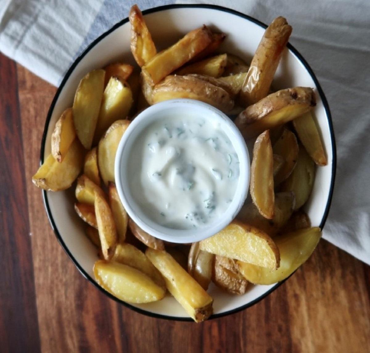 Eine Schale mit Pommes. In der Mitte steht eine kleine Schüssel mit einem Kräuterdip.