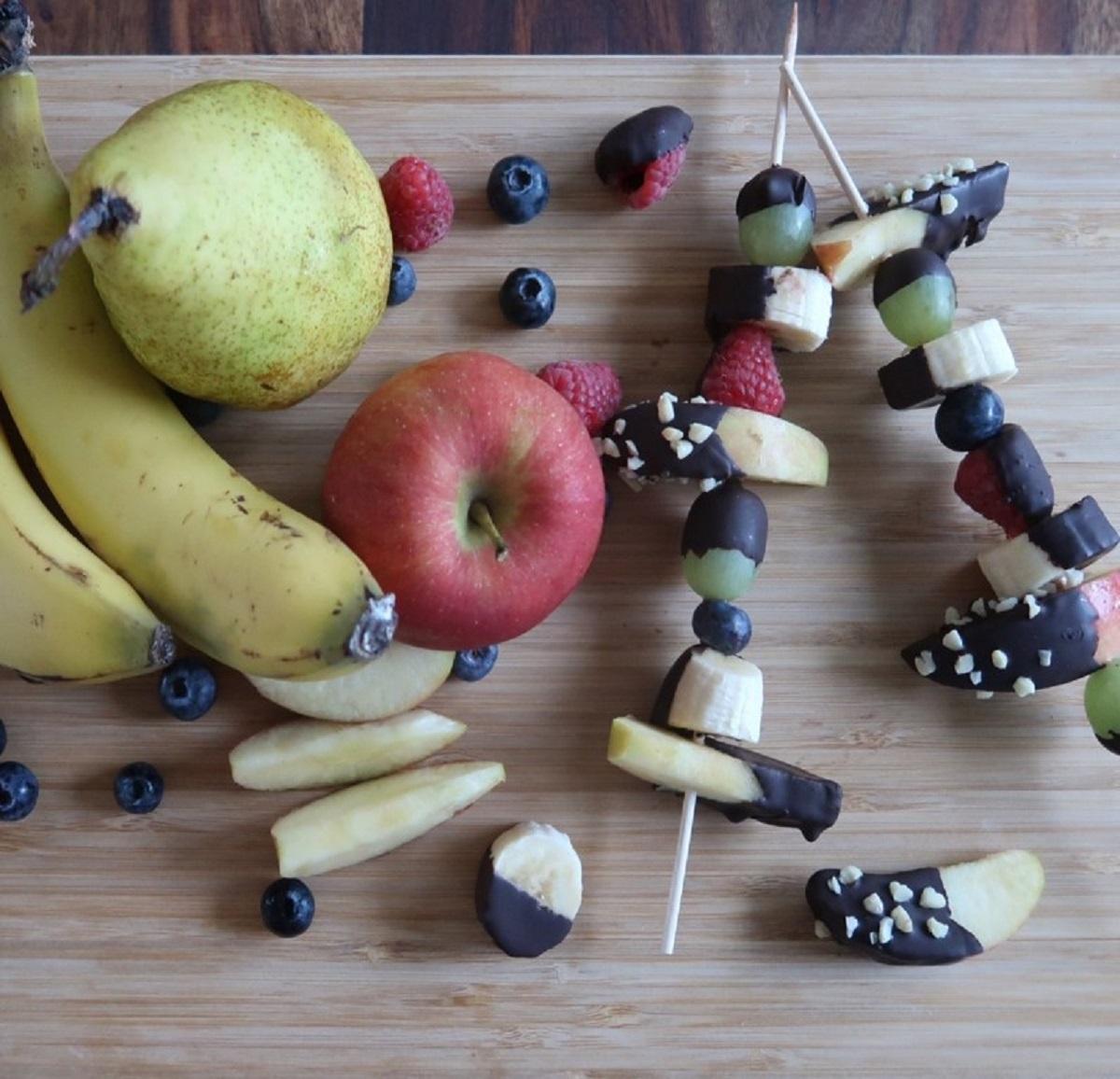 Schokoalden-Obst-Spieße. Daneben liegen noch frische Birnen, Bananen und Äpfel.