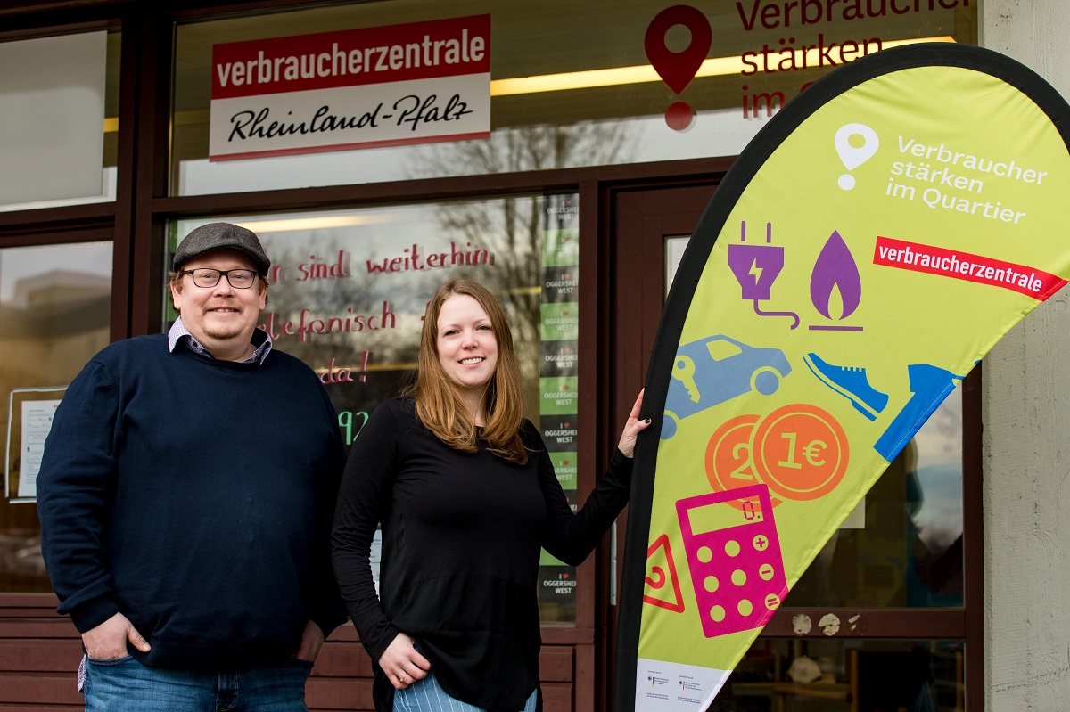 Zwei Personen stehen an eienr Fahne und lächeln in die Kamera