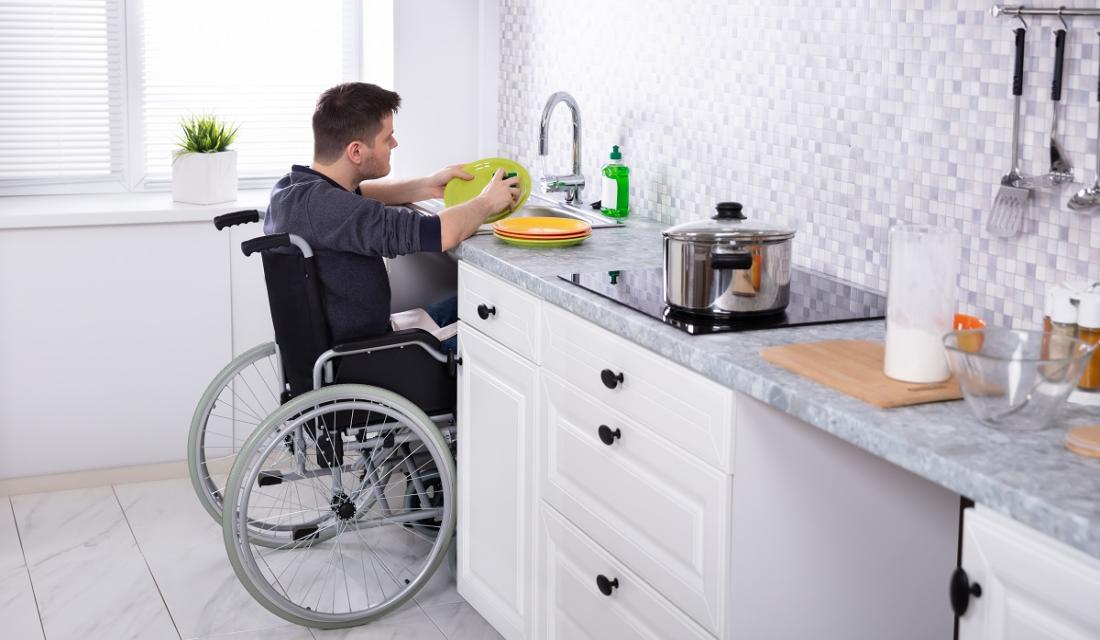 Ein Mann im Rollstuhl spült in seiner Küche Geschirr.