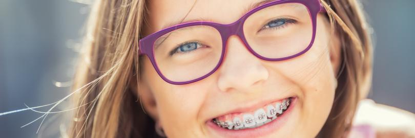 Lächelndes Mädchen mit lila Brille und Zahnspange