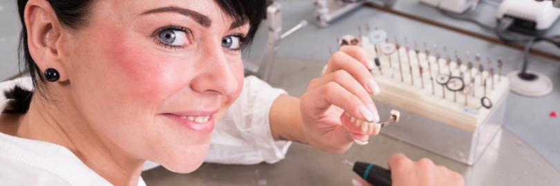 Zahntechnikerin im Dentallabor im Ausland stellt Zahnersatz her, sie bearbeitet eine Teilprothese für die Zähne.