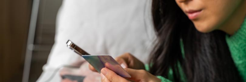 Eine junge Frau kauft etwas über ihr Handy und bezahlt mit Kreditkarte