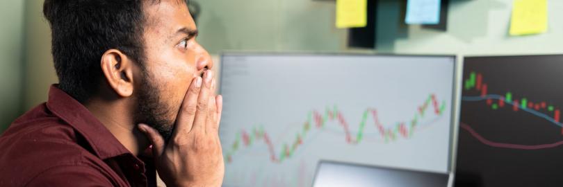 Mensch sitzt vor Computerbildschirmen mit Trading-Kurven und ist schockiert