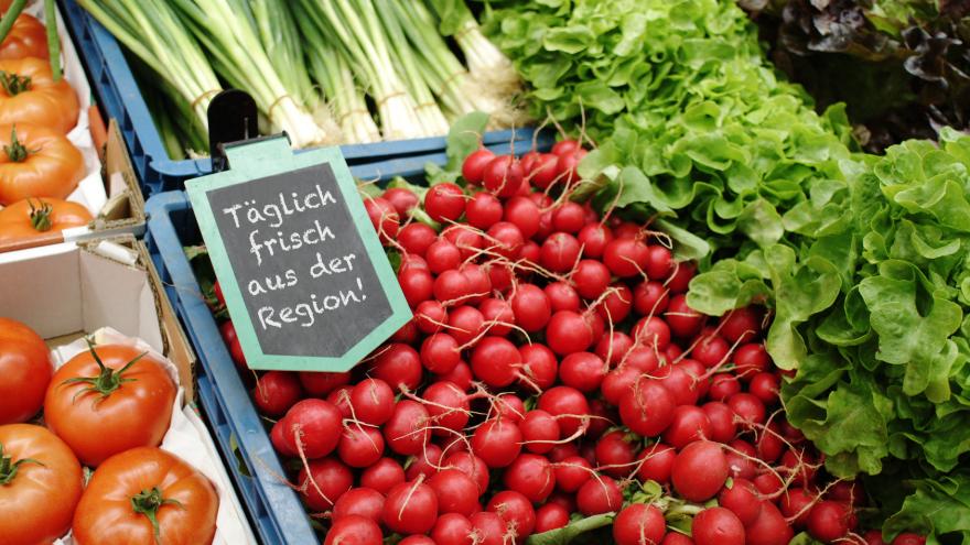 Auf einem Marktstand liegen Gemüse und Salate aus, ein Schild weist auf regionale Hersteller hin.