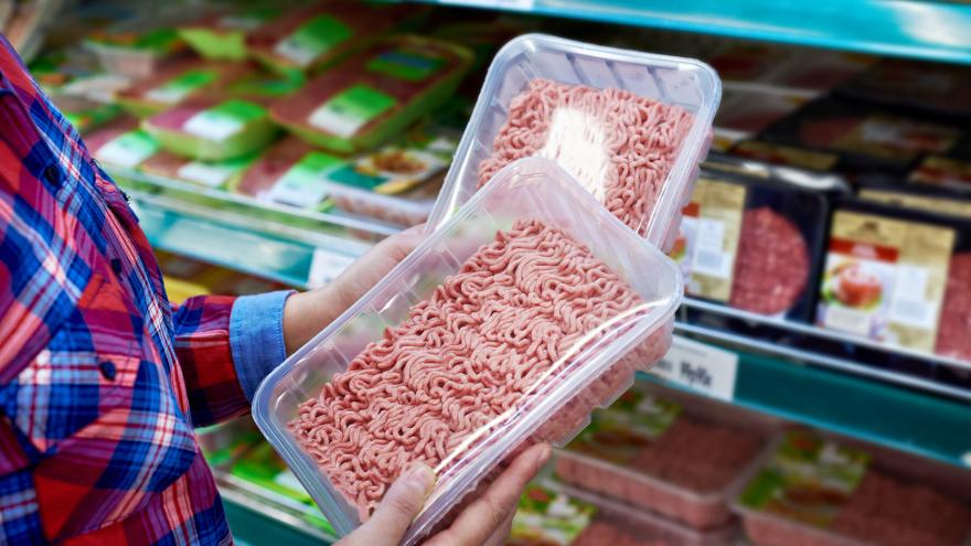 Jemand kauft im Supermarkt ein und hält zwei Packungen Hackfleisch in der Hand.