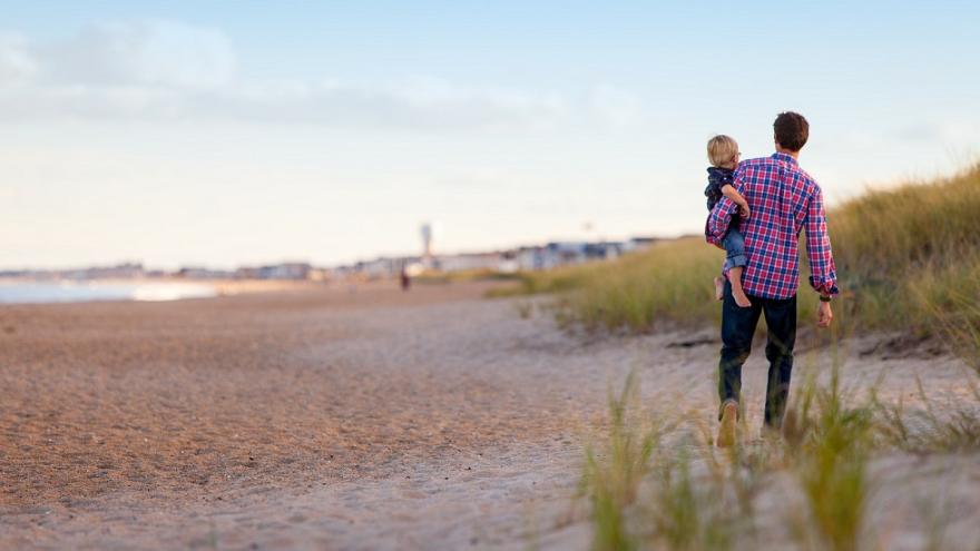 Vater mit Sohn auf dem Arm am Strand.