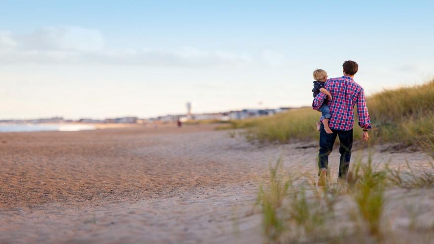 Vater mit Sohn auf dem Arm am Strand.