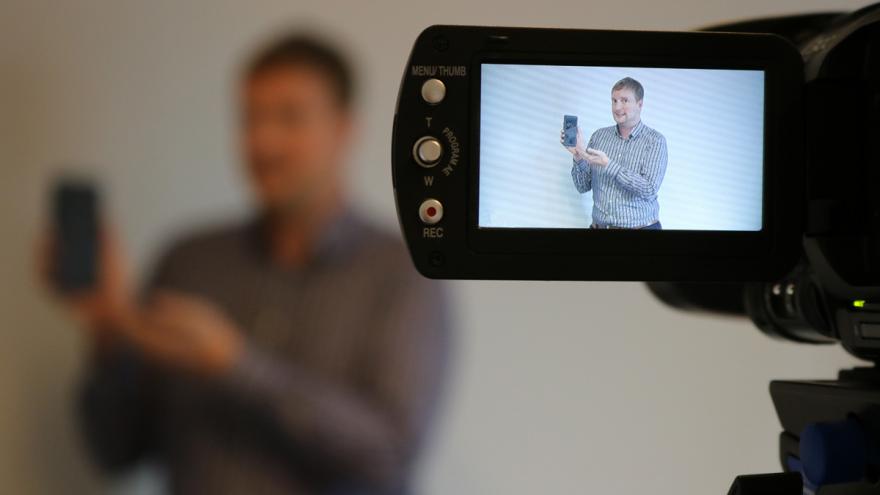 Ein Mann zeigt ein Smartphone in eine Videokamera.