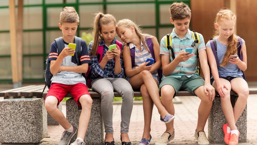 Kinder auf Bank mit Smartphones in den Händen.