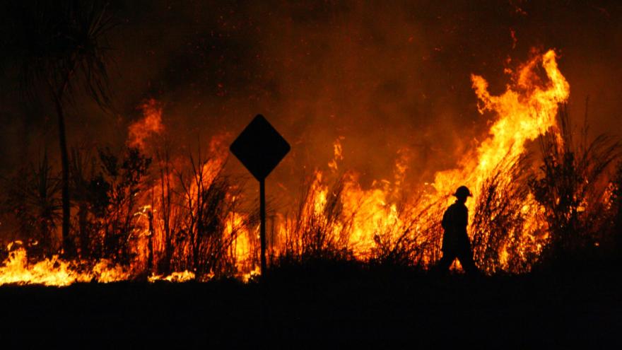 Ein Feuerwehrmann läuft vor einem großen Feuer.