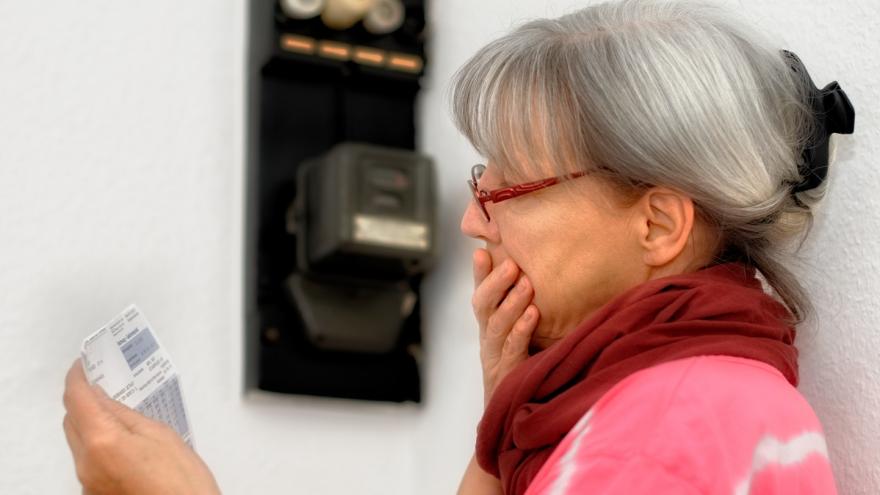 Frau steht mit Rechnung am Stromzähler.