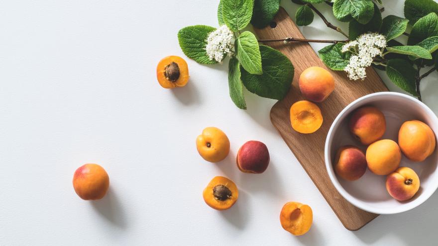 Am rechten unteren Bild steht eine weiße Schale mit orange-roten Aprikosen auf einem Holzbrett. Um das Holzbrett herum liegen weitere, auch aufgeschnittene Aprikosen und einige Aprikosenzweige mit grünen Blättern und weißen Blüten.