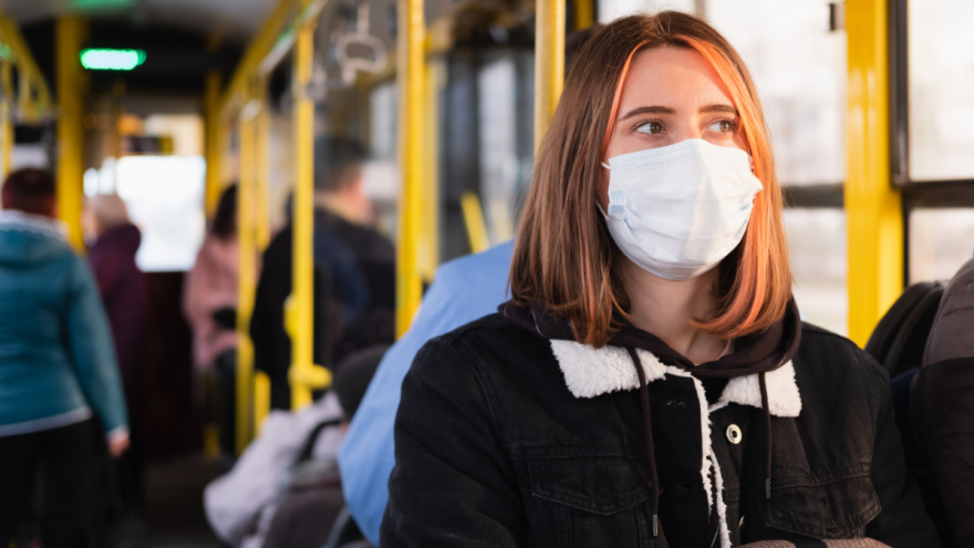Eine Frau sitzt in einem Bus und  trägt eine Schutzmaske.