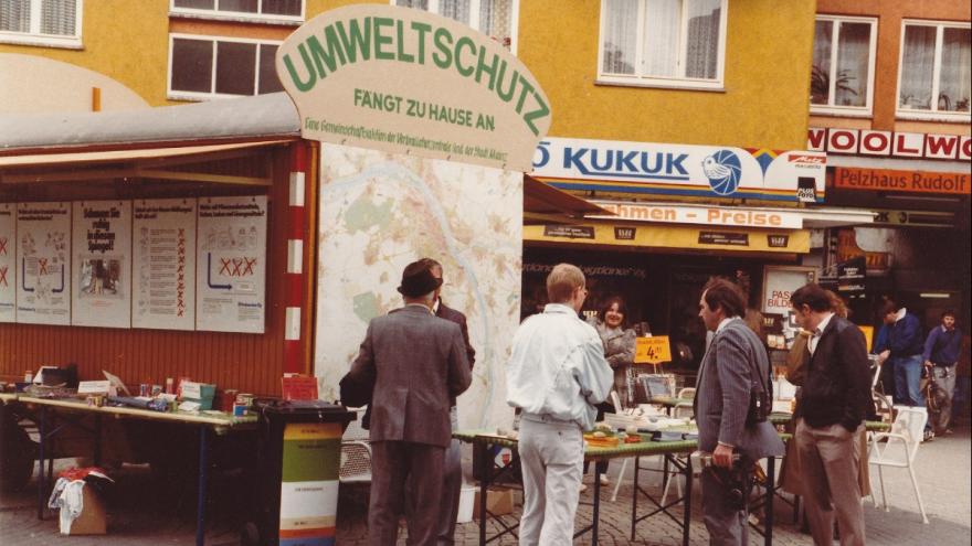 Menschen stehen an einem Bauwagen, der zu einem Infostand umfunktioniert wurde. 