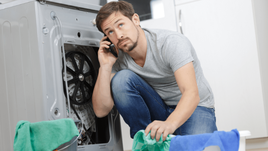Ein Mann kniet vor der Rückseite einer Waschmaschine und telefoniert.