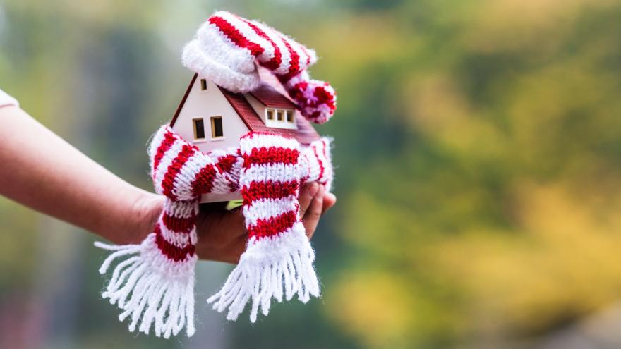 Ein kleines Haus mit einem Schal umwickelt auf einer Hand.