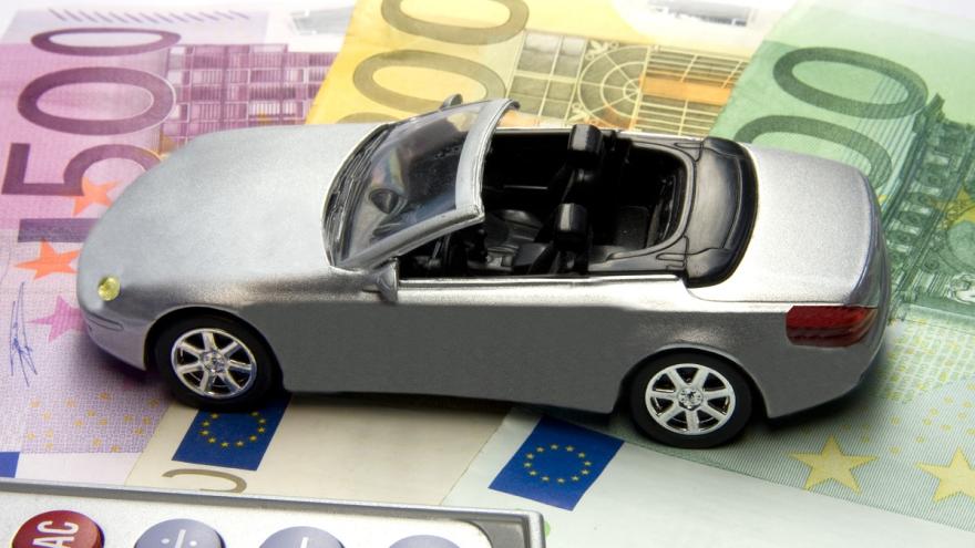 Ein Spielzeugauto steht auf verschiedenen Geldscheinen. Am unteren Bildrand ist ein Ausschnitt eines Taschenrechners zu sehen.