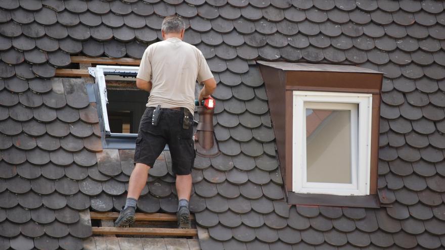 Mann steht auf einem Dach und repariert Ziegel.