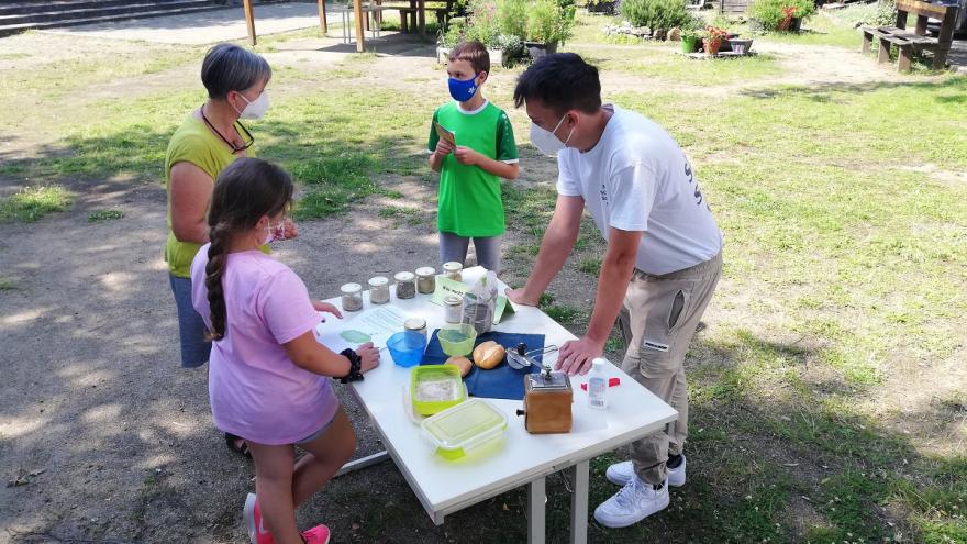 Drei Kinder und eine Erwachsene stehen an einem Tisch mit verschiedenen Materialien.