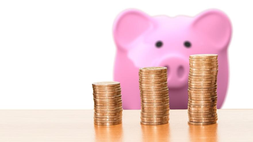 Drei kleine Türme aus Kleingeld und im Hintergrund ein Sparschwein.