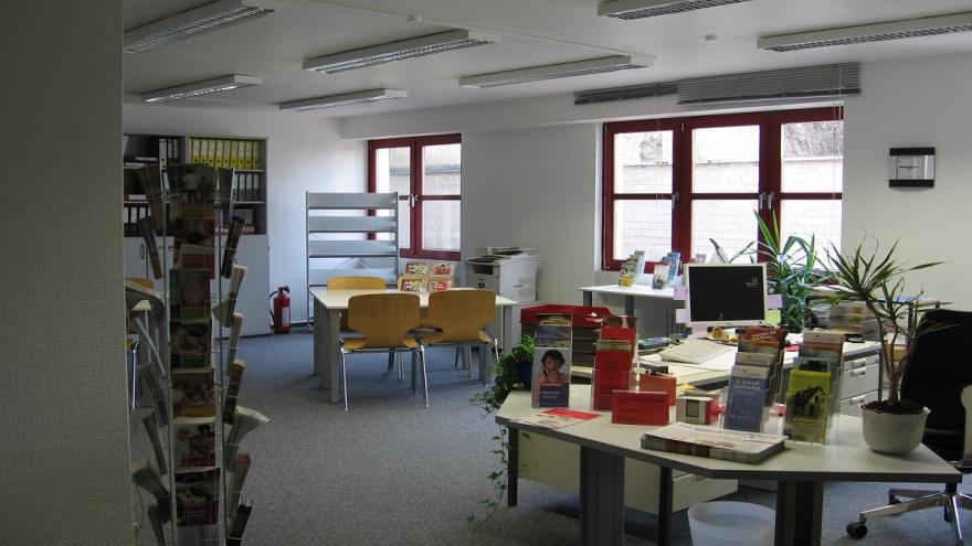 Ein menschenleerer Büroraum mit Schreibtischen und Prospektständern.