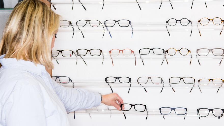 Eine Frau steht beim Optiker vor einer großen Auswahl an Brillen.