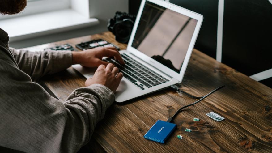 Ein Mann sitzt vor einem Laptop, an dem eine externe Festplatte angeschlossen ist. Neben der Festplatte liegen verschiedene Speicherkarten.