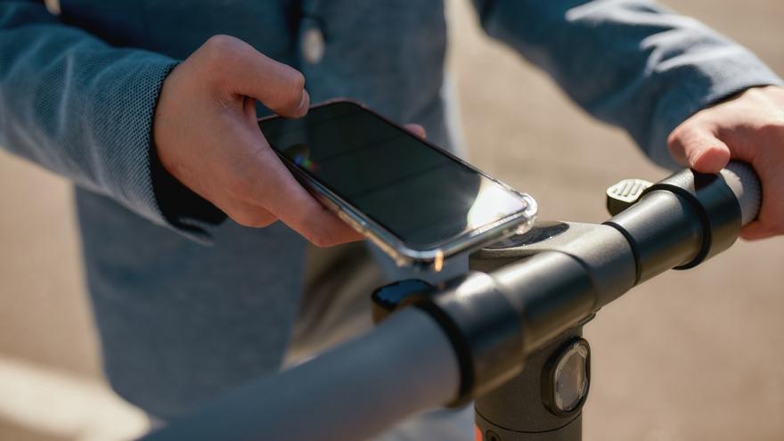 Eine Person hält sein Smartphone an einen E-Roller.