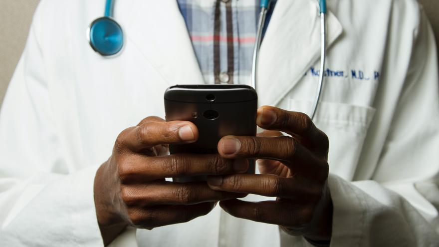 Ein Arzt mit Stetoskop und weißem Kittel hält ein Handy in seinen Händen.