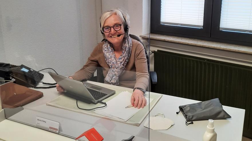 Eine Frau sitzt an einem Bürotisch und lächelt in die Kamera.