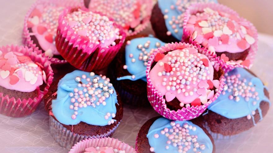 Muffins mit buntem Zuckerguss und Zuckerstreuseln auf einem Tisch.