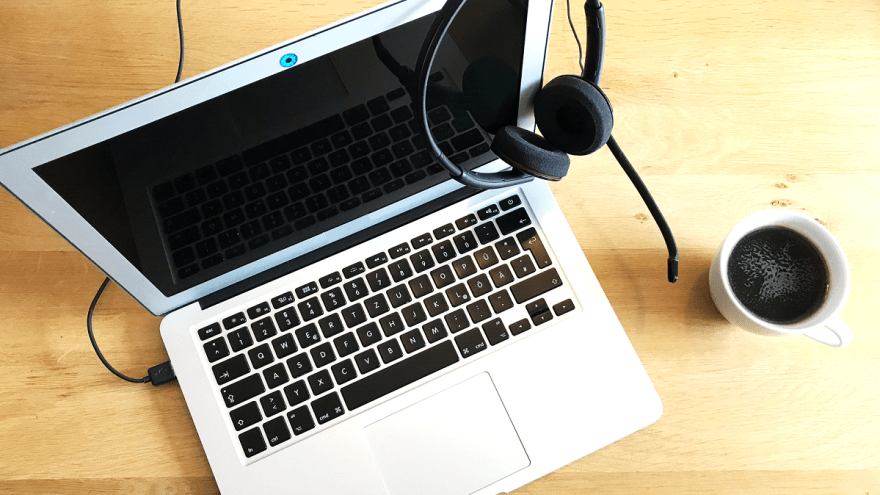 Ein Laptop mit Kopfhörern und eine Kaffeetasse stehen auf einem Tisch.