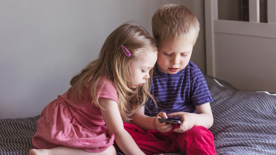Zwei kleine Kinder sitzen auf dem Sofa und schauen in ein Smartphone.