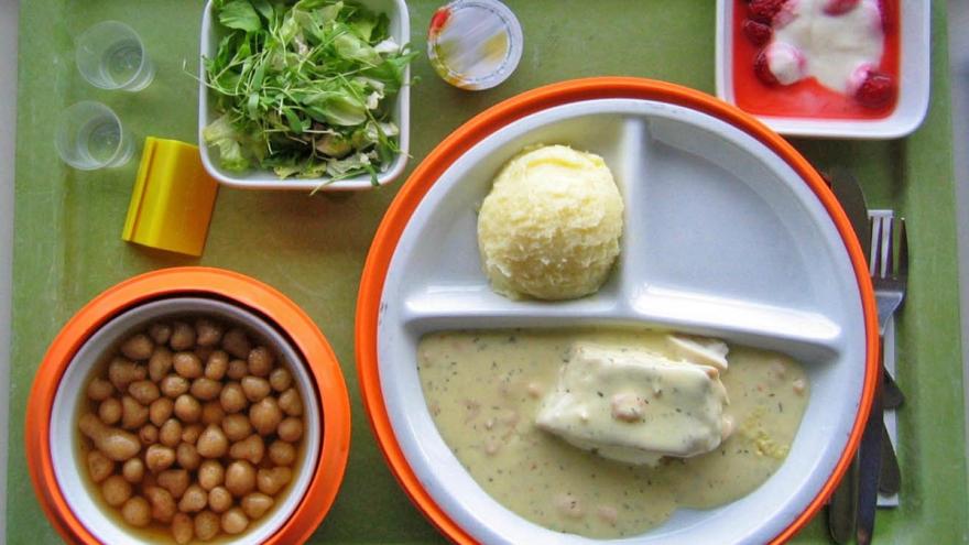 Ein Krankenhaustablett mit verschiedenen, portionierten Essensgängen drauf und zwei Gläsern Wasser.