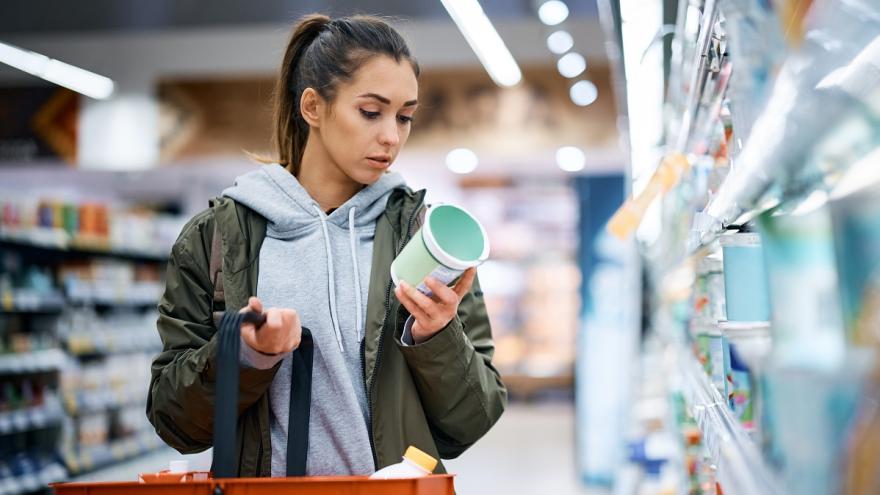 Eine Frau steht im Supermarkt und schaut kritisch auf eine Verpackung eines Lebensmittel. 