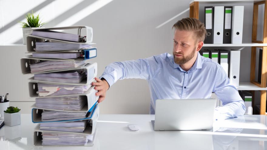 Ein Mann sitzt am Schreibtisch, neben sich ein Stapel Aktenordner.