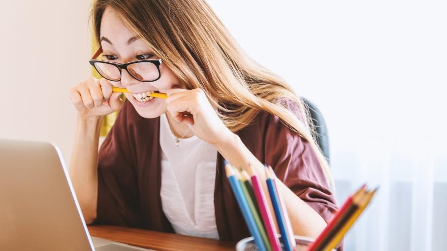 Eine Frau sitzt vor dem Laptop und beißt verzweifelt auf einen Bleistift.