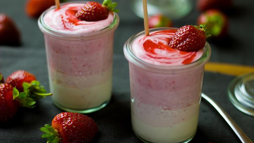 Zwei Gläser mit selbsgemachten Erbeerjoghurt und frischen Erdbeeren auf einem Tisch.